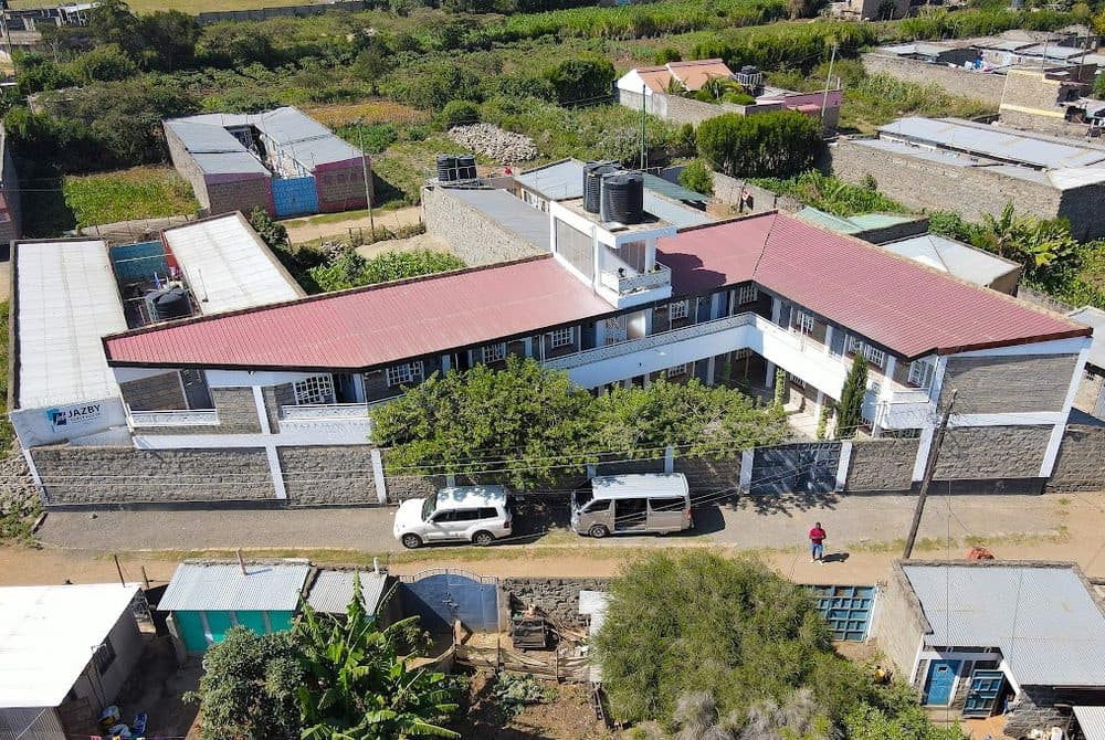 Aerial view of Jazby Guest House in Naivasha, a two-storey building with a red roof and a sign on the left, with two vehicles parked on the street in front