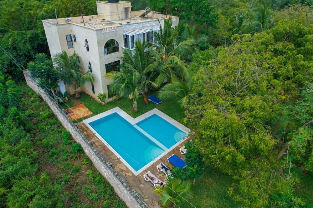 Aerial view of Silent Palms Villa in Diani, a cream-coloured villa with a turquoise swimming pool and sun loungers surrounded by palms and trees